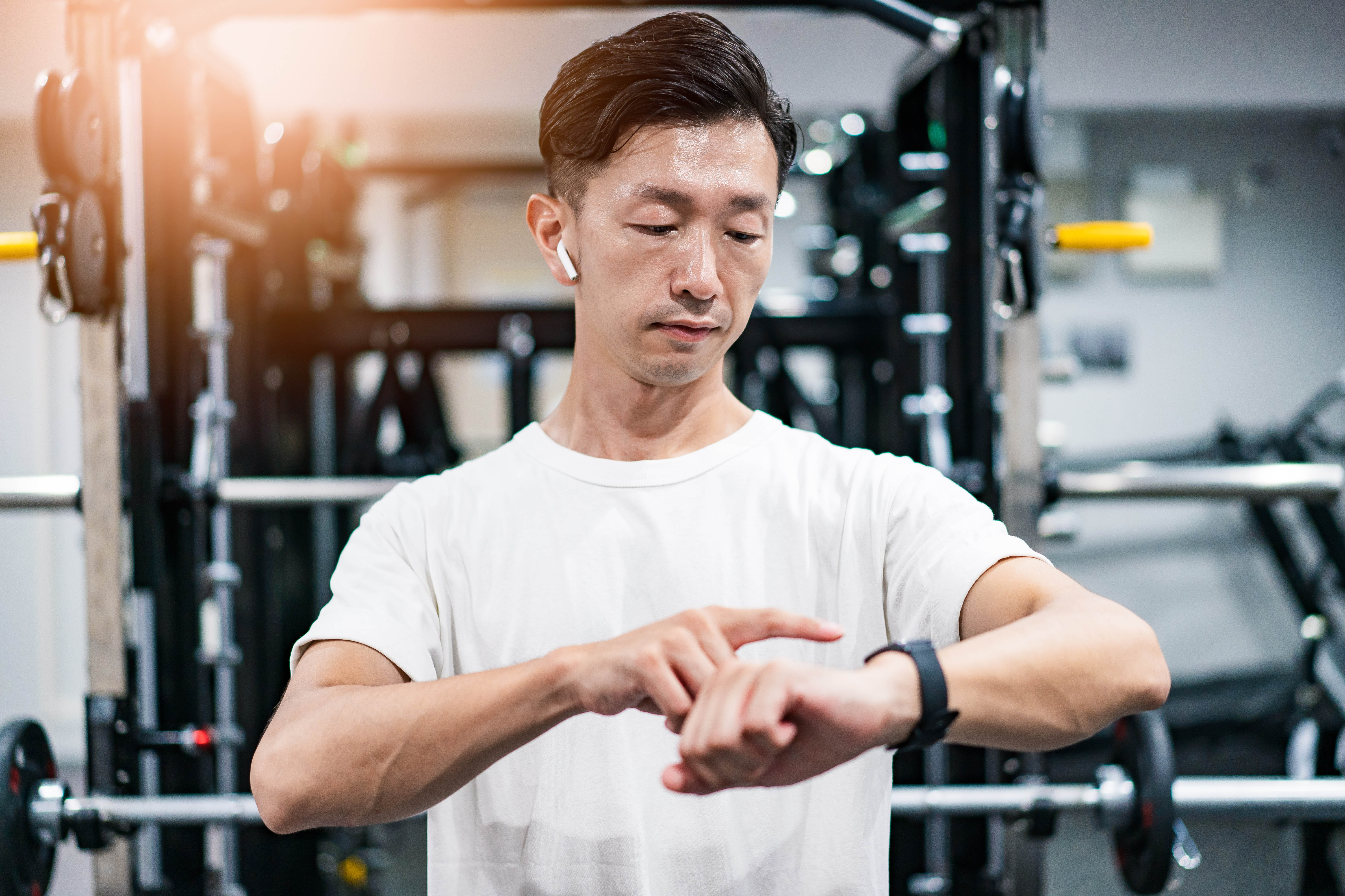 Middle aged Asian man in the gym checking his smart watch. He also has his headphones in. Middle aged Asian man in the gym checking his smart watch. He also has his headphones in.